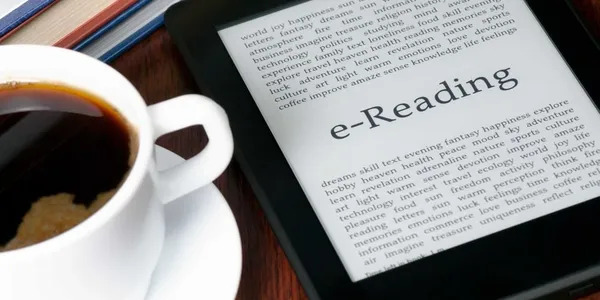 A coffee cup and an e-reader on a table.